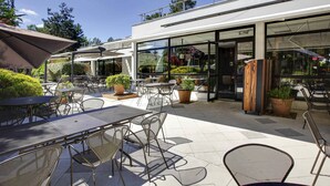 An outdoor patio area with tables and chairs, potted plants, and a glass storefront.