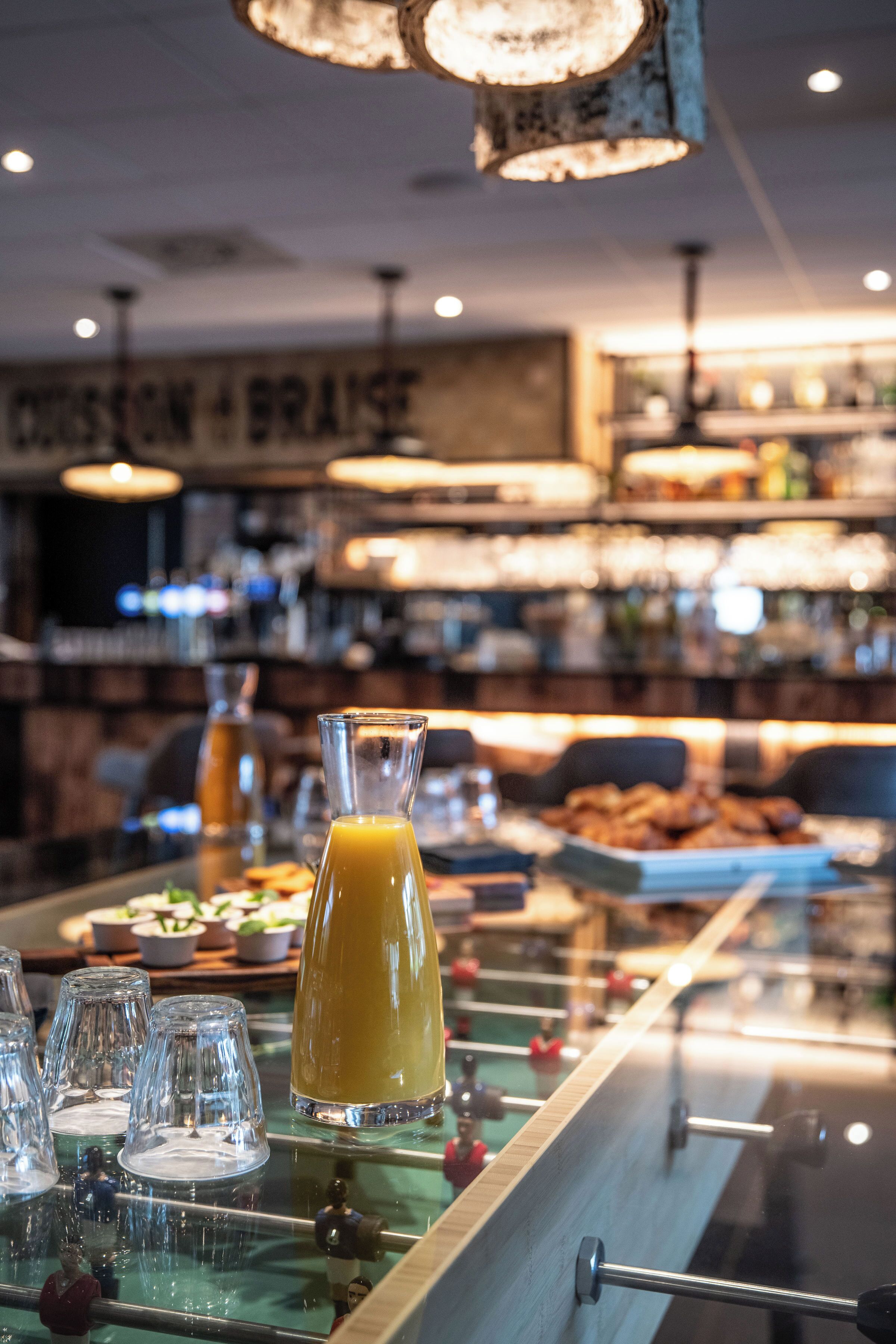 A bar area with a glass pitcher of orange juice, several glasses, and a variety of food items on a counter.