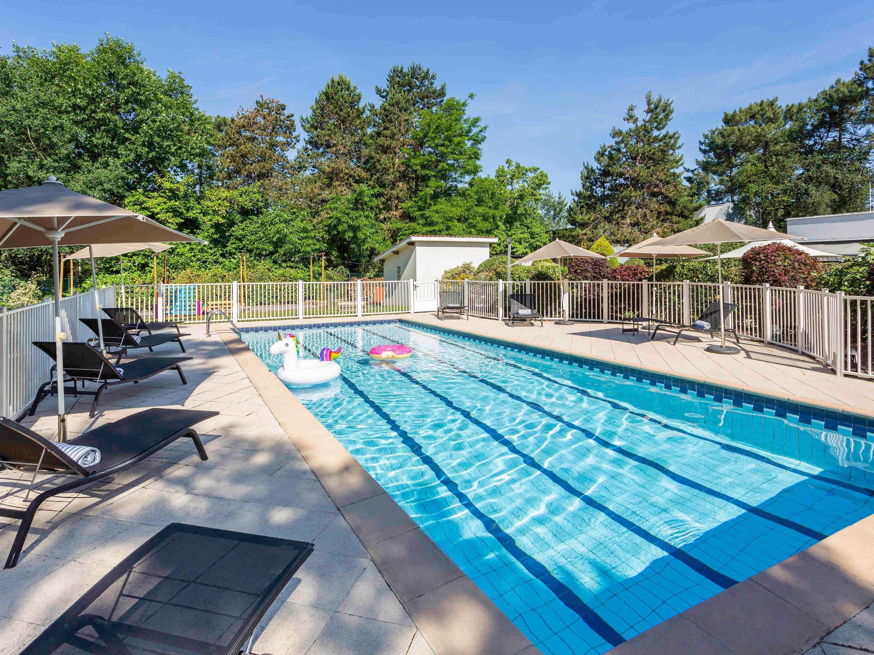 A swimming pool with lounge chairs and umbrellas, surrounded by a white fence and trees.