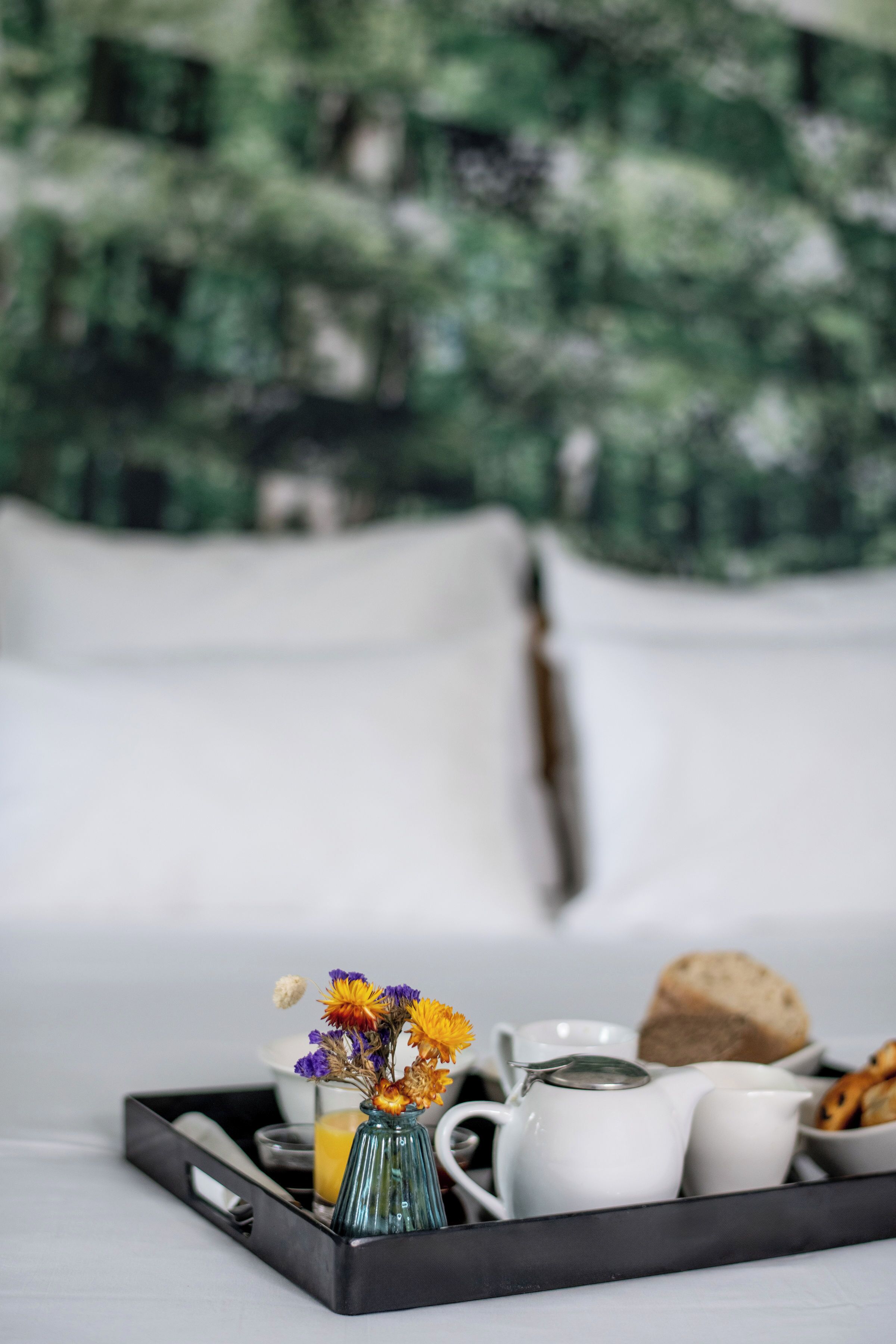 A tray with breakfast items including a vase of flowers, a teapot, cups, and bread.