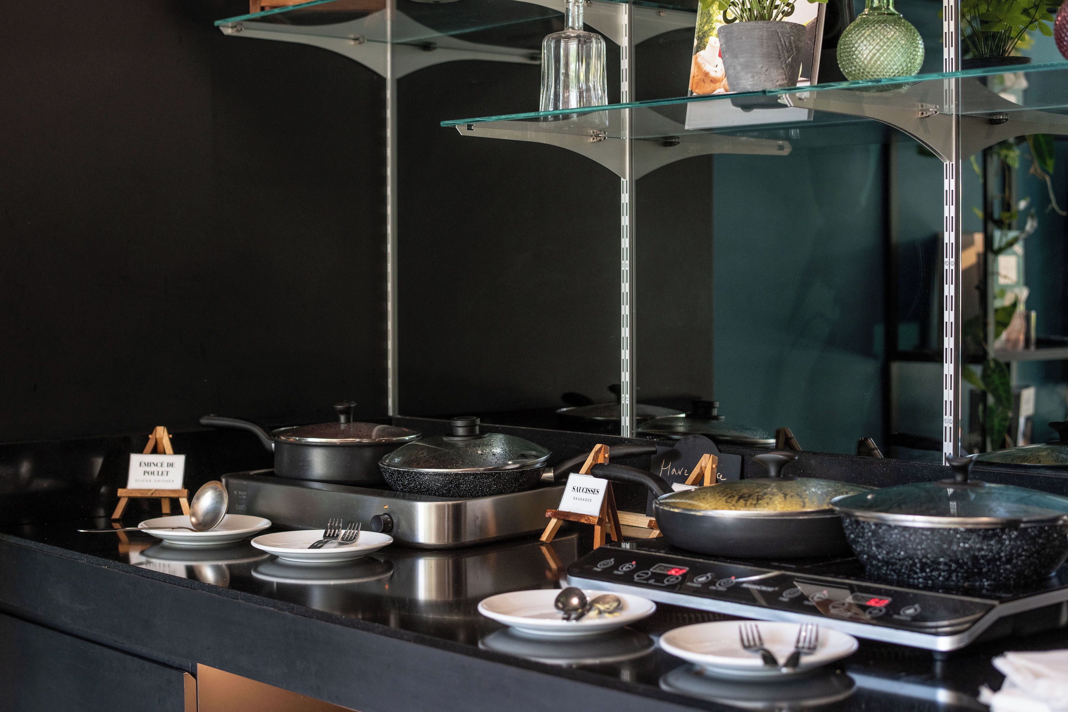 A buffet setup with multiple cooking stations, each labeled with a dish name.