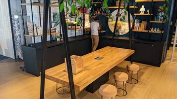Un interior moderno con una mesa y taburetes de madera, rodeado de estanterías con diversos objetos y plantas.