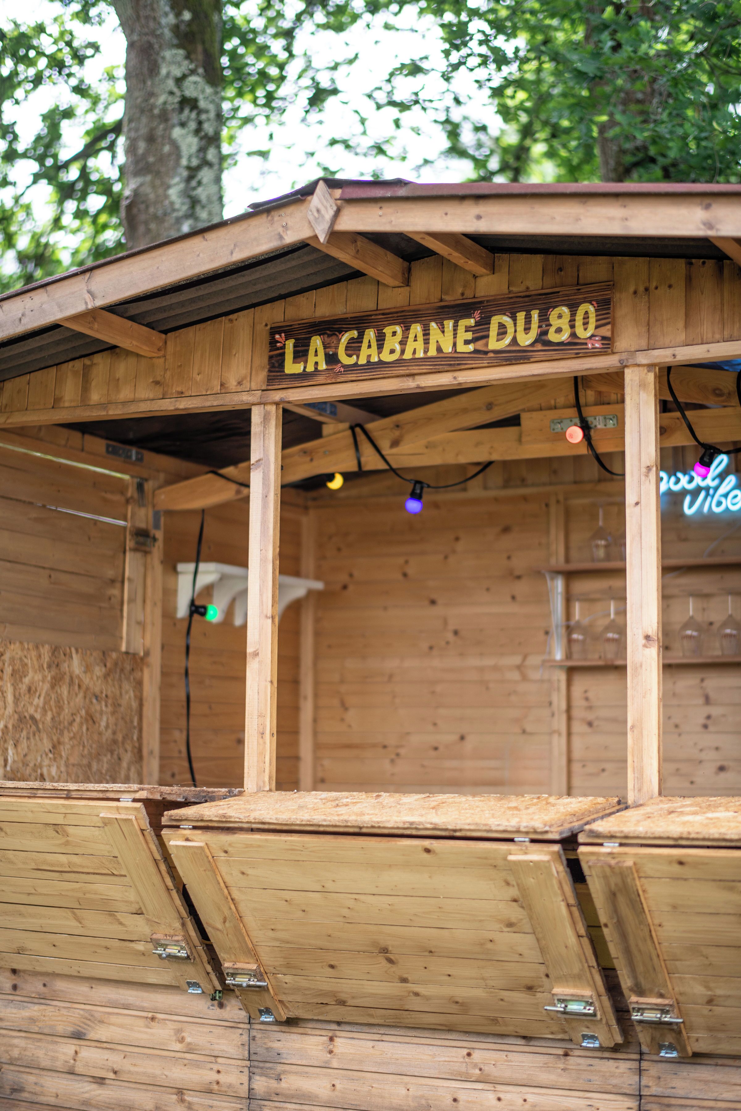 Une structure en bois sur laquelle est apposée une enseigne indiquant « LA CABANE DU 80 ».