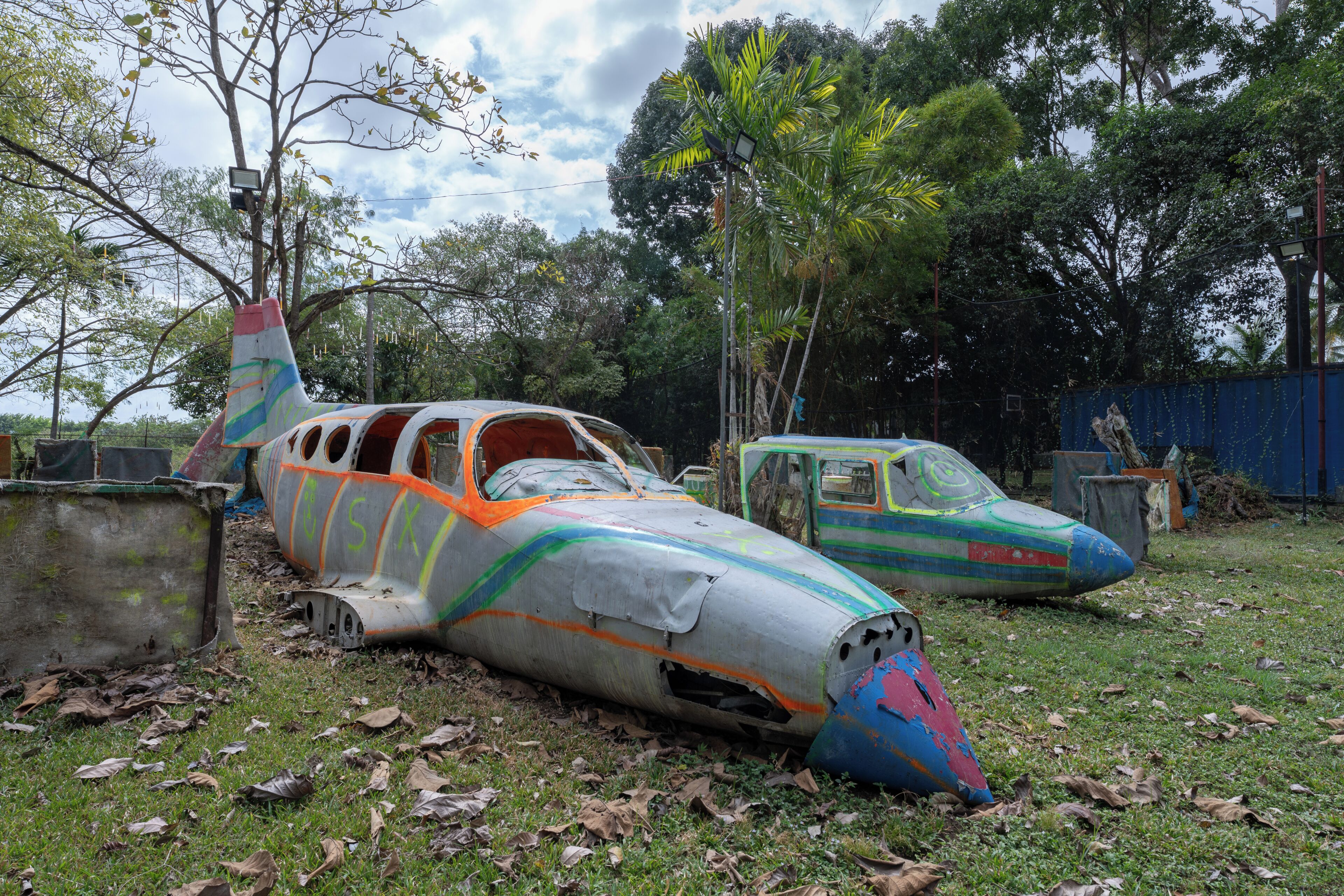 A damaged airplane with colorful paint, lying on grass surrounded by trees.