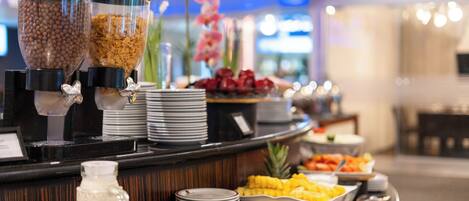 A buffet counter with various food options, including cereal, fruits, and a beverage dispenser.