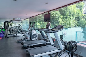 Ein Fitnessstudio mit verschiedenen Trainingsgeräten, darunter Laufbändern und Kraftmaschinen, und einem großen Fenster mit Blick auf Bäume.