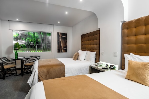 Ein Hotelzimmer mit zwei Betten, einem kleinen Tisch mit Stühlen, einem Fenster mit Blick auf Bäume und einem an der Wand befestigten Telefon.