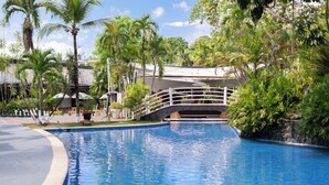 Una piscina con un puente, rodeada de palmeras y un edificio de techo inclinado.