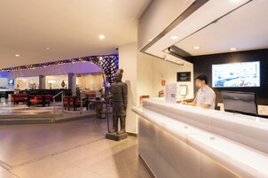 Un área de recepción con recepcionista, una estatua y una pantalla digital.