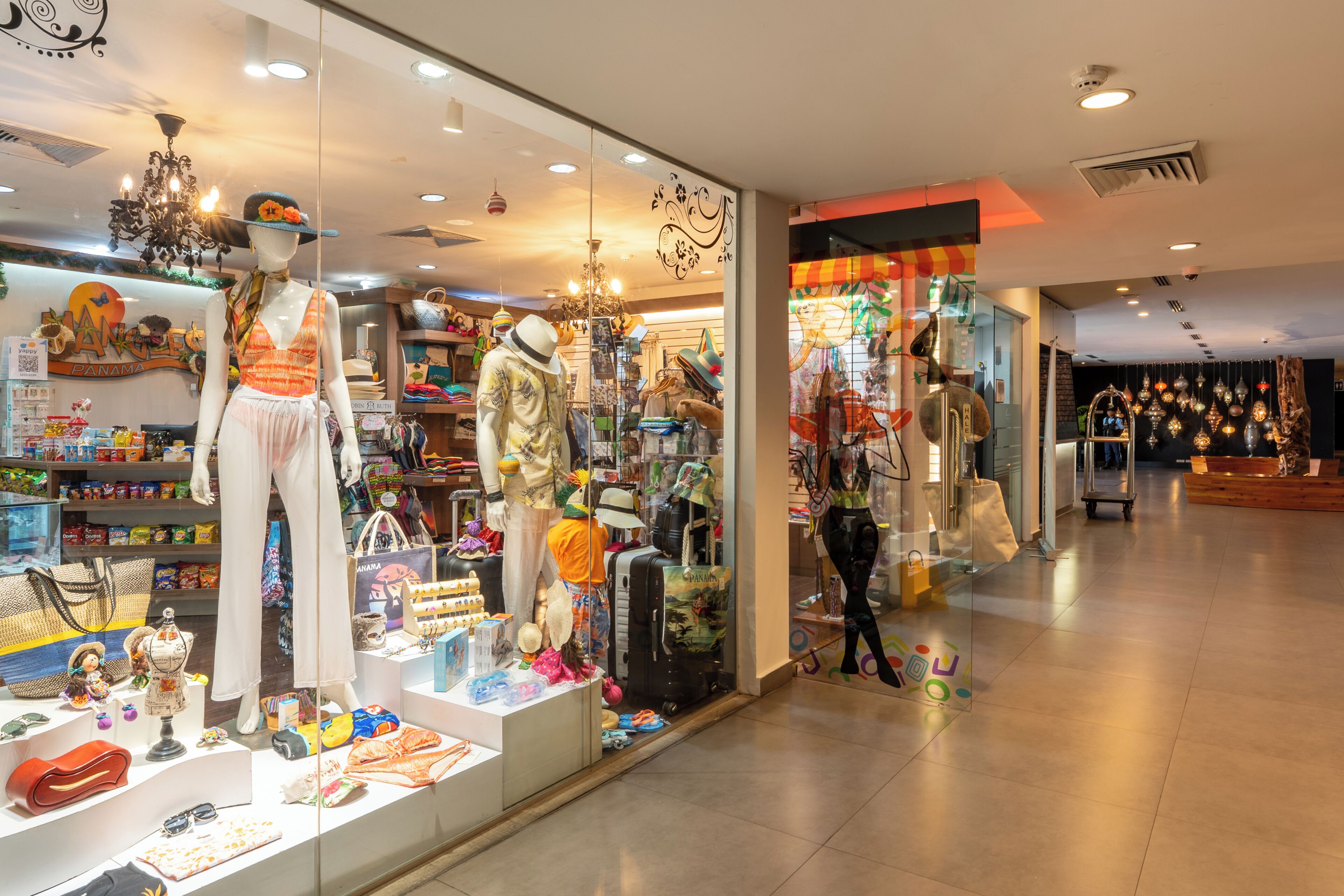 A store with mannequins displaying clothing and accessories, shelves with bags and hats, and a variety of travel-related items.
