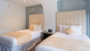 Habitación de hotel con dos camas, una mesita de noche con teléfono y una lámpara fijada a la pared.
