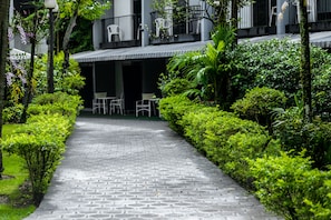 Uma trilha pavimentada leva a um edifício com área externa para sentar e vegetação exuberante.