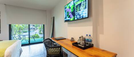 A hotel room with a bed, a desk with a laptop, a TV on the wall, and a view of the outdoors.