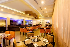 Um restaurante amplo com várias mesas e cadeiras, área de bar e design moderno no teto.
