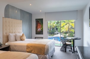 Ein modernes Hotelzimmer mit einem großen Bett, einem kleinen Schreibtisch, einem Stuhl und einem Balkon mit Blick auf einen Pool.