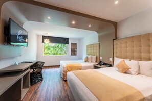 A hotel room with two beds, a desk, a television, and a window with a view of greenery. - Riande Aeropuerto Hotel & Casino (Tocumen)
