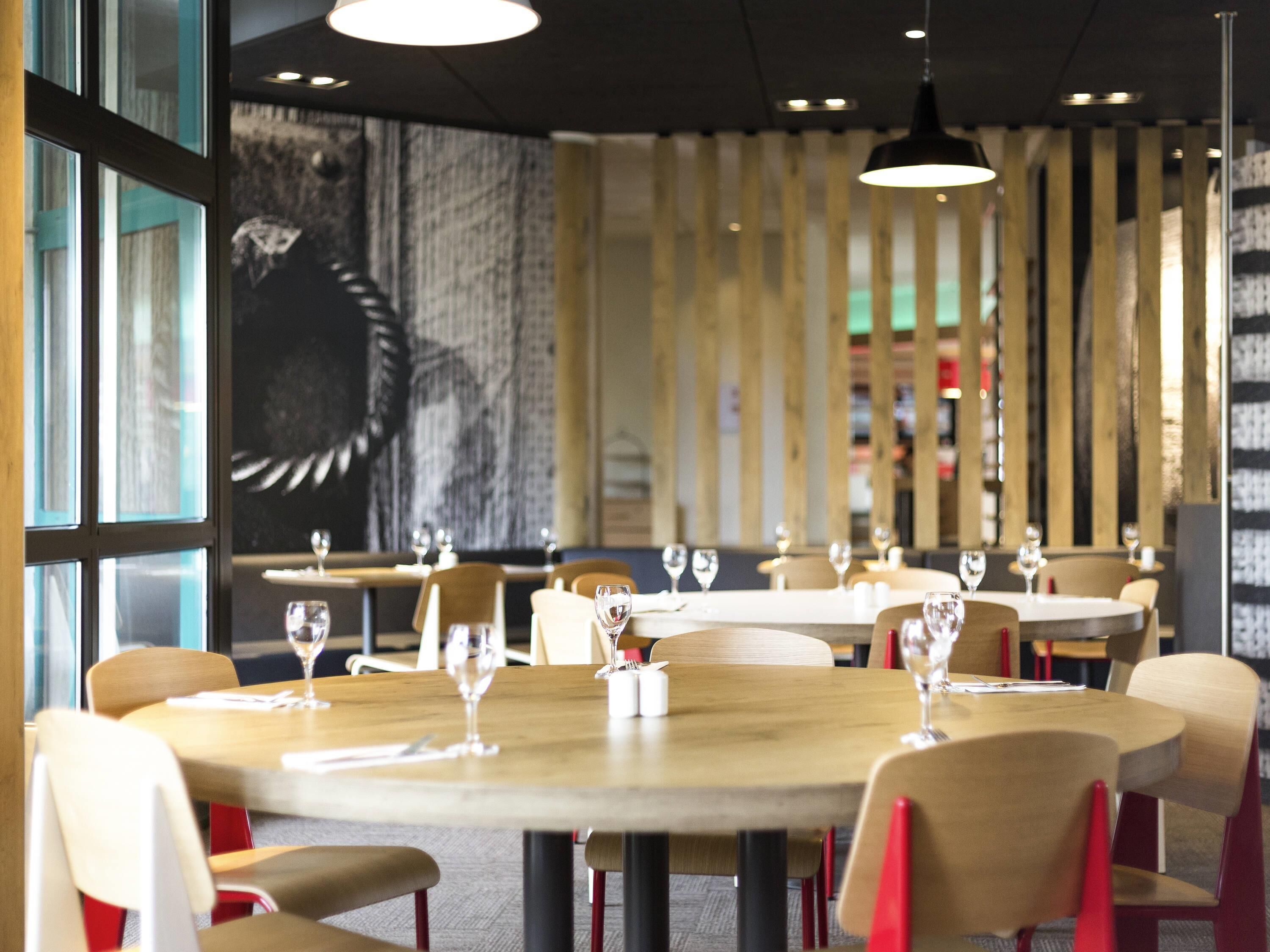 A restaurant with round tables, chairs, and hanging pendant lights.
