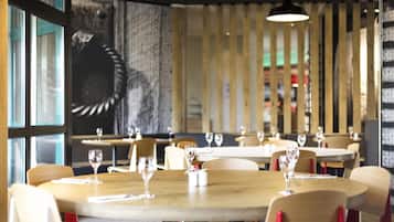 A restaurant with round tables, chairs, and hanging pendant lights.