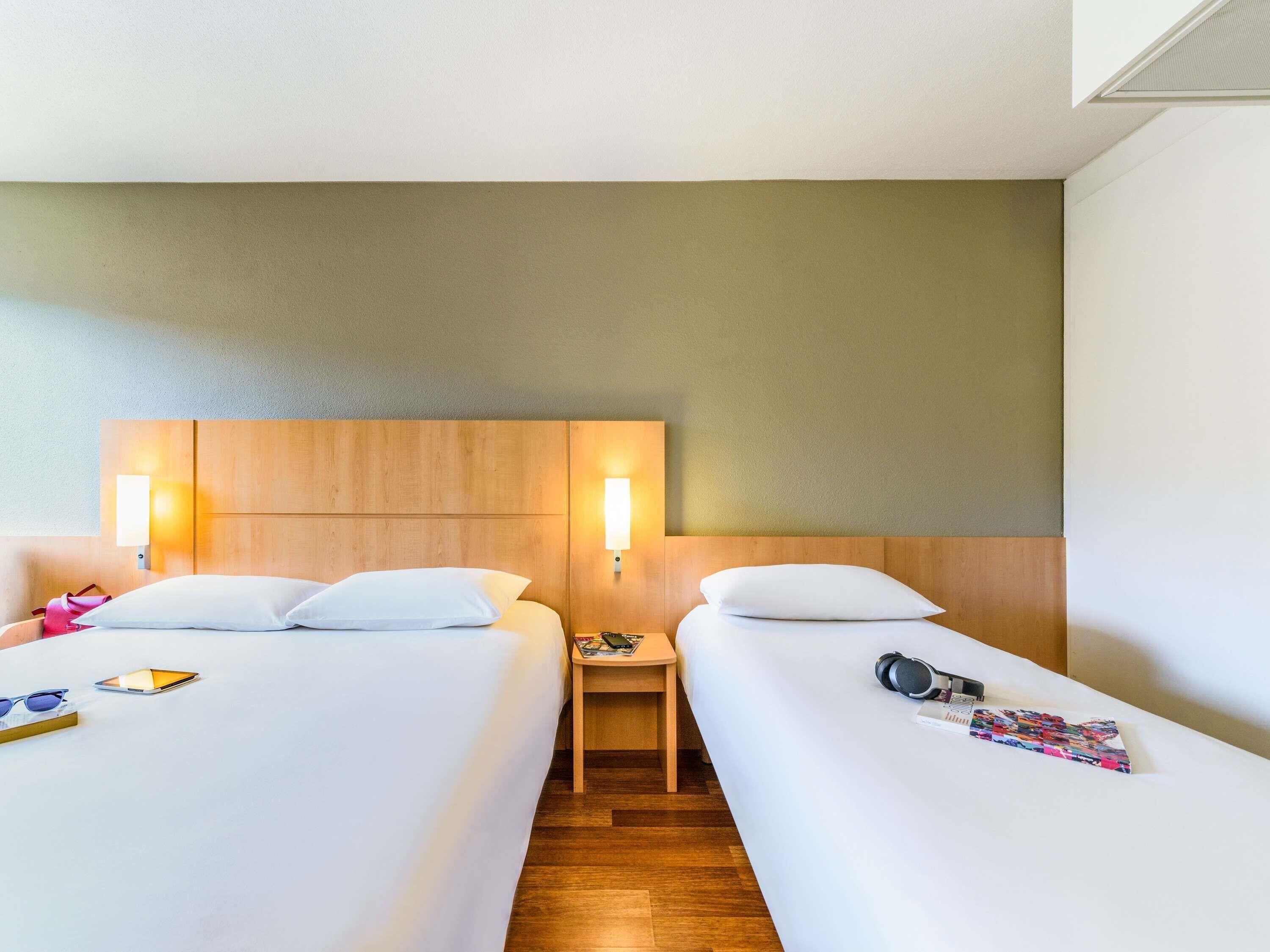 Une chambre d’hôtel avec deux lits, des têtes de lit en bois, des tables de chevet et des lampes fixées au mur.