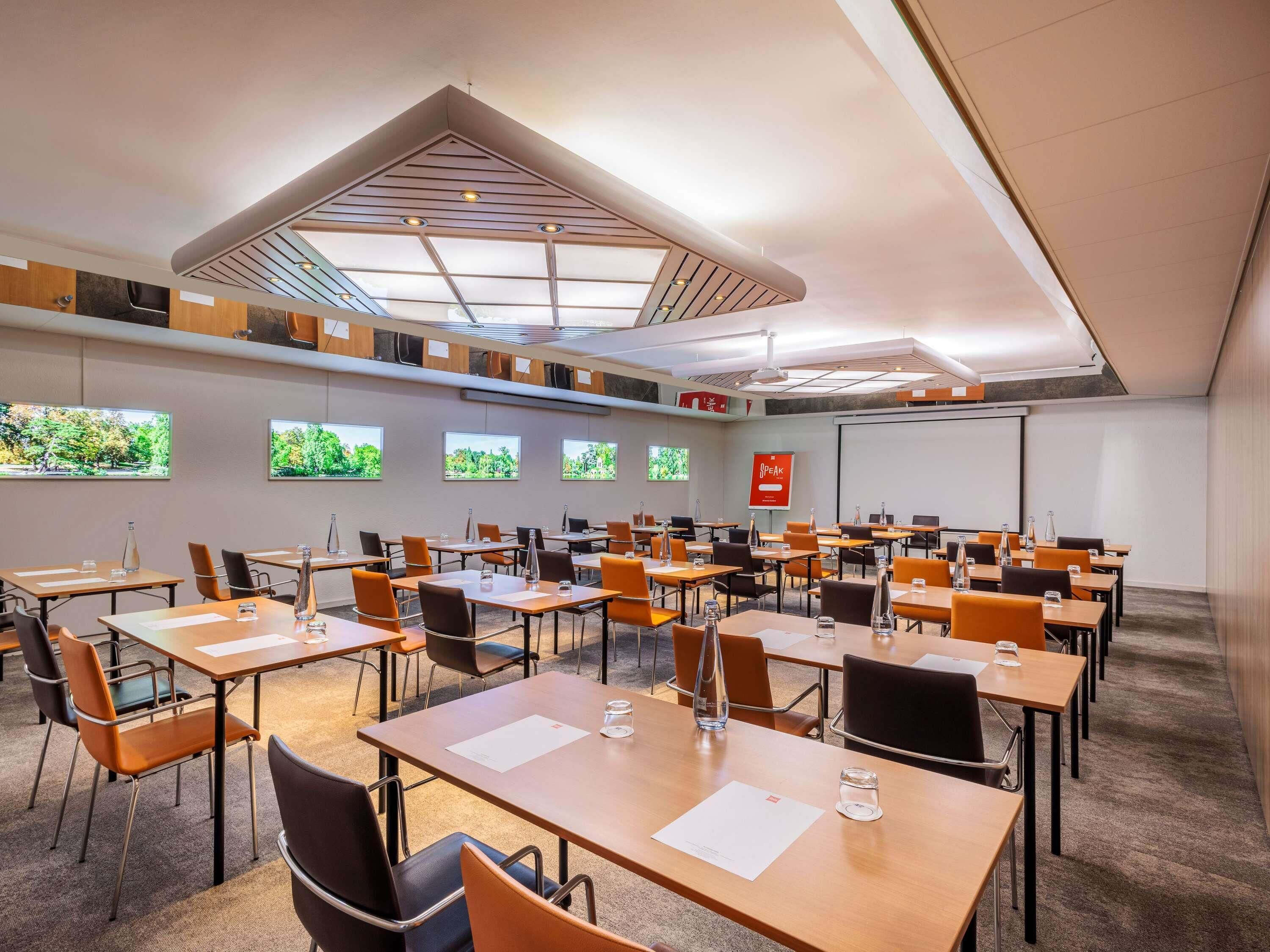 A conference room with multiple tables, chairs, and a large screen.
