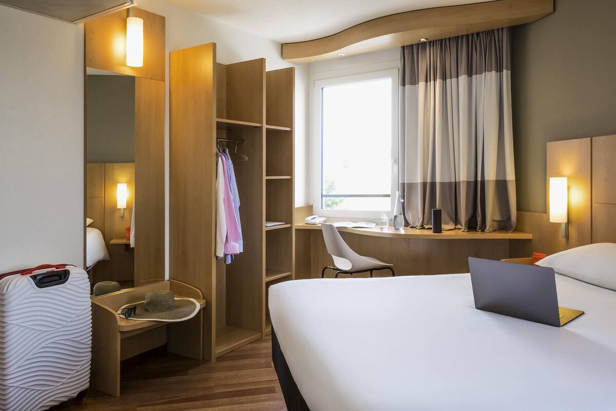 Una habitación de hotel con cama, escritorio, silla, armario y maleta.