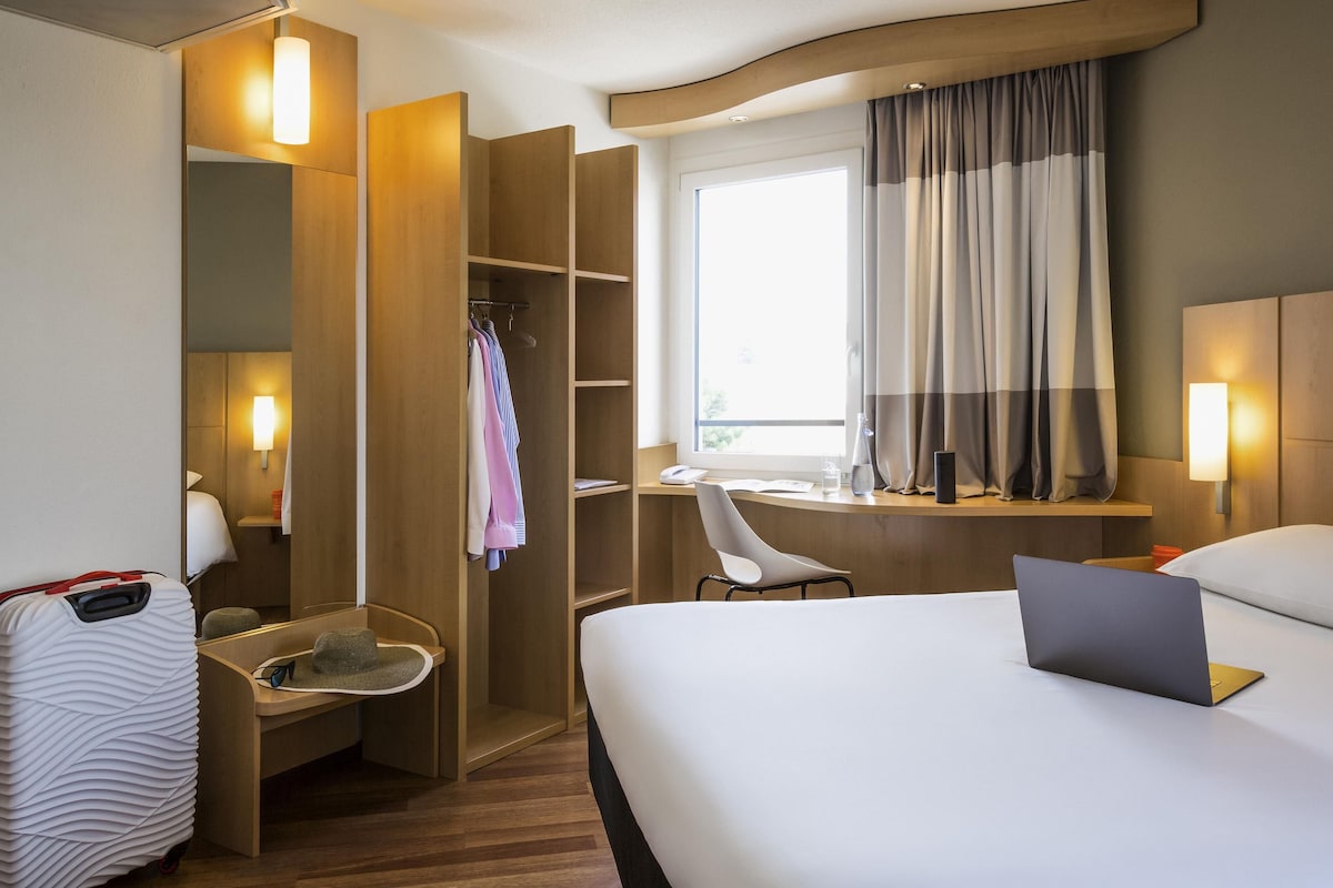 A hotel room with a bed, a desk, a chair, a wardrobe, and a suitcase.