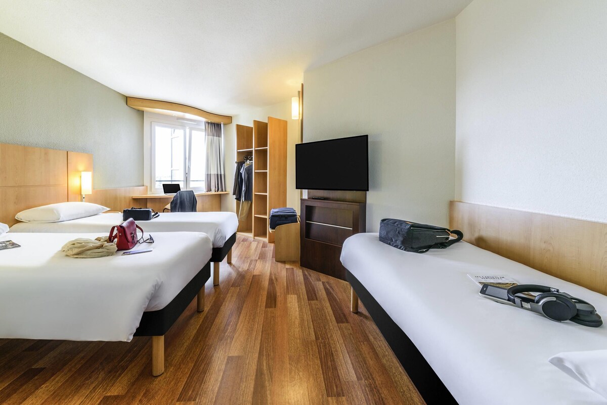 A hotel room with two beds, a TV, a desk with a laptop, and a wardrobe.