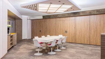 Ein Konferenzraum mit langem Tisch und weißen Stühlen, einer Holzwand als Raumteiler und einer Decke mit Oberlichtern.