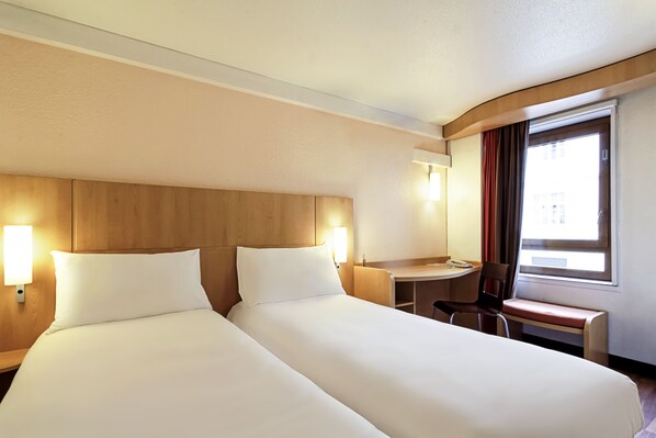 Habitación de hotel con dos camas, un escritorio, una silla y un ventanal con cortinas.