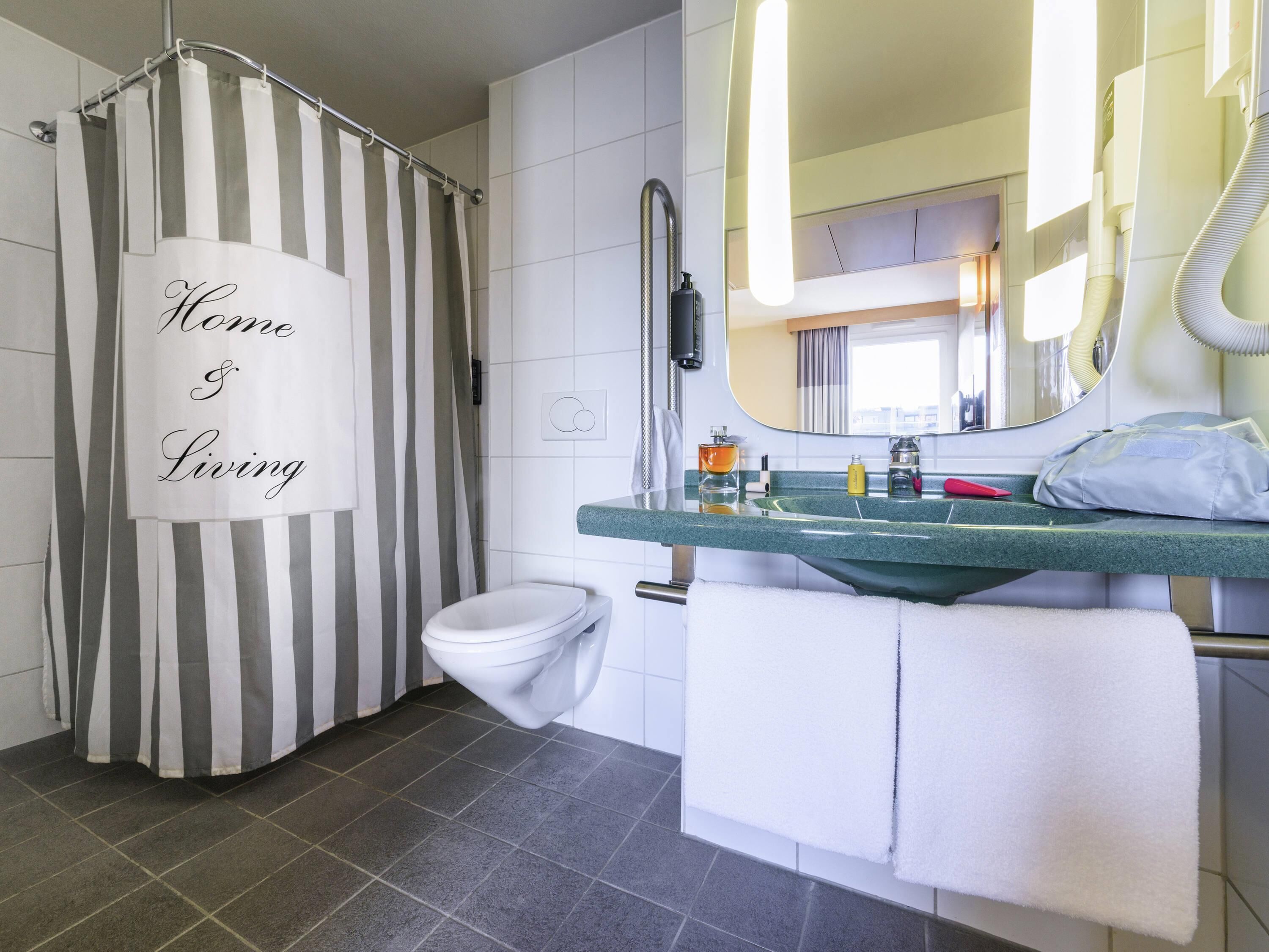 A bathroom with a striped shower curtain, a toilet, a sink with a mirror, and a towel rack.