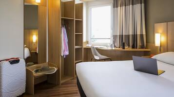A hotel room with a bed, a desk, a chair, a wardrobe, and a suitcase.