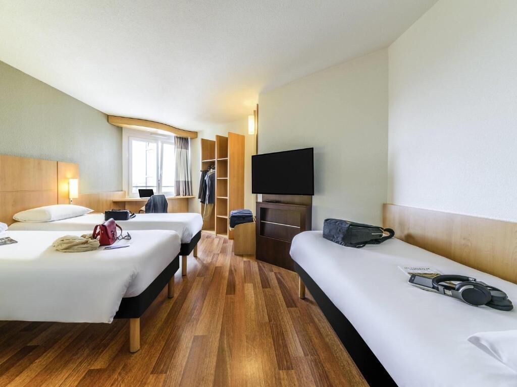 A hotel room with two beds, a TV, a wardrobe, and a window.