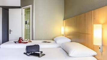 A hotel room with two beds, a door, a wall-mounted light, and a bag on the bed.