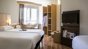 Habitación de hotel con dos camas, un escritorio, televisor y armario.