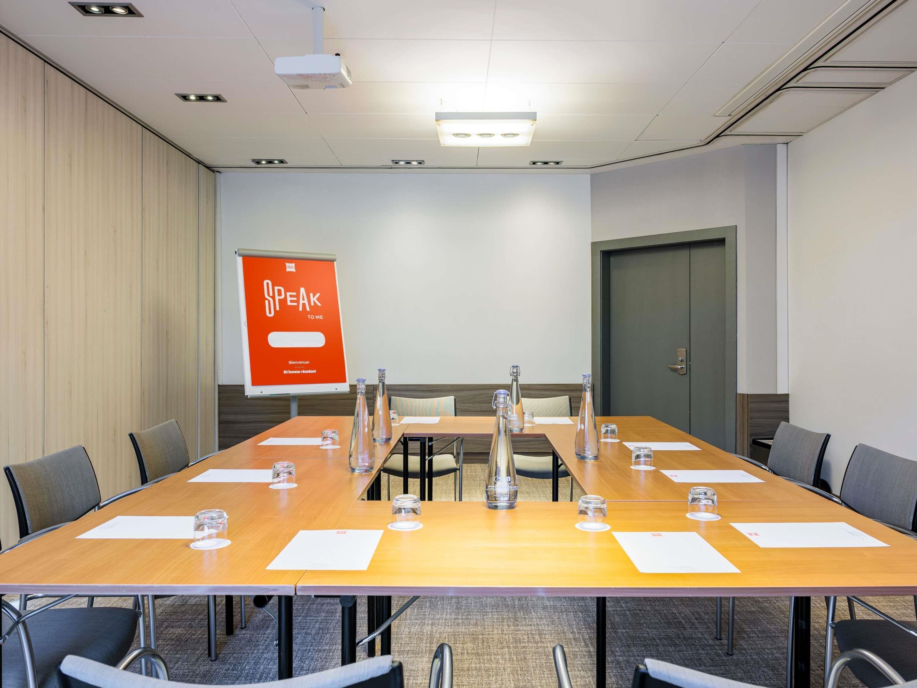 A conference room with a long table, chairs, a projector, a whiteboard, and a door.