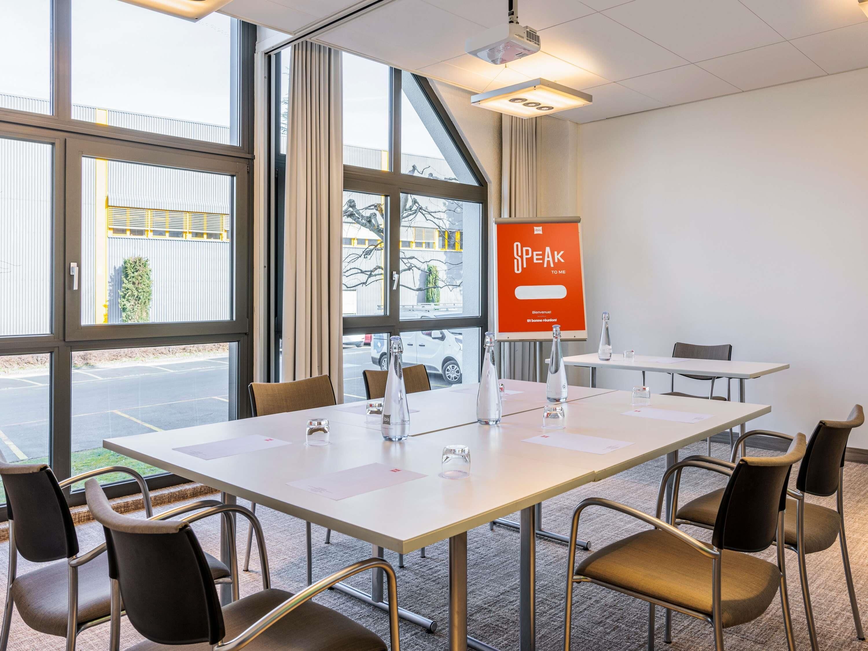 A conference room with a large table, chairs, a projector, and a 'Speak to Me' sign.