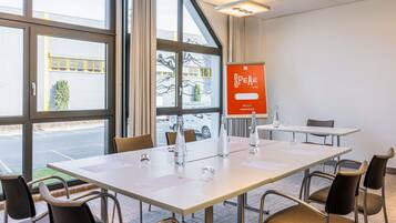 A conference room with a large table, chairs, a projector, and a 'Speak to Me' sign.