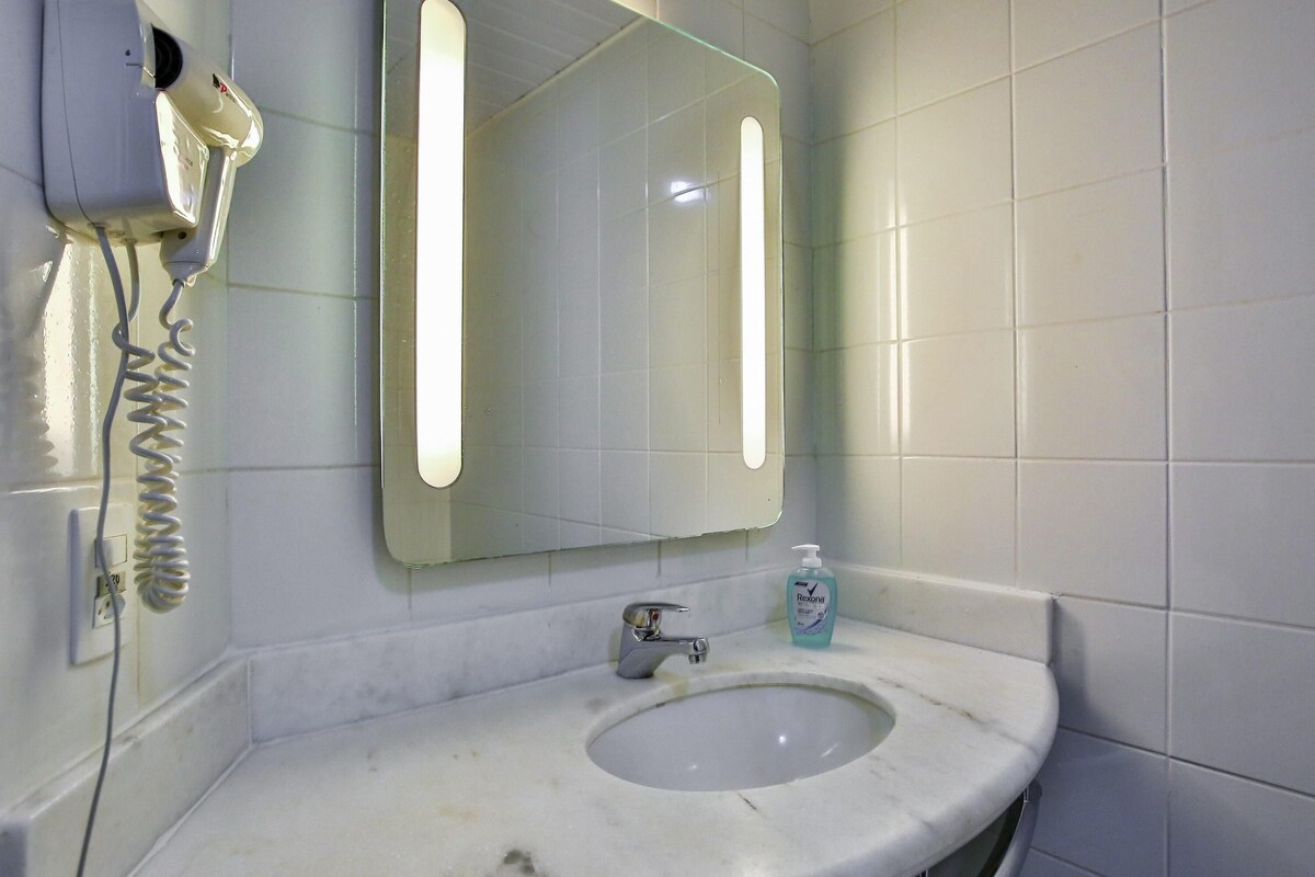 A bathroom with a white sink, a mirror, and a hairdryer mounted on the wall.