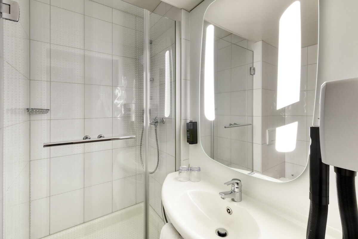 A modern bathroom with a glass shower enclosure, a white sink, and a large mirror.