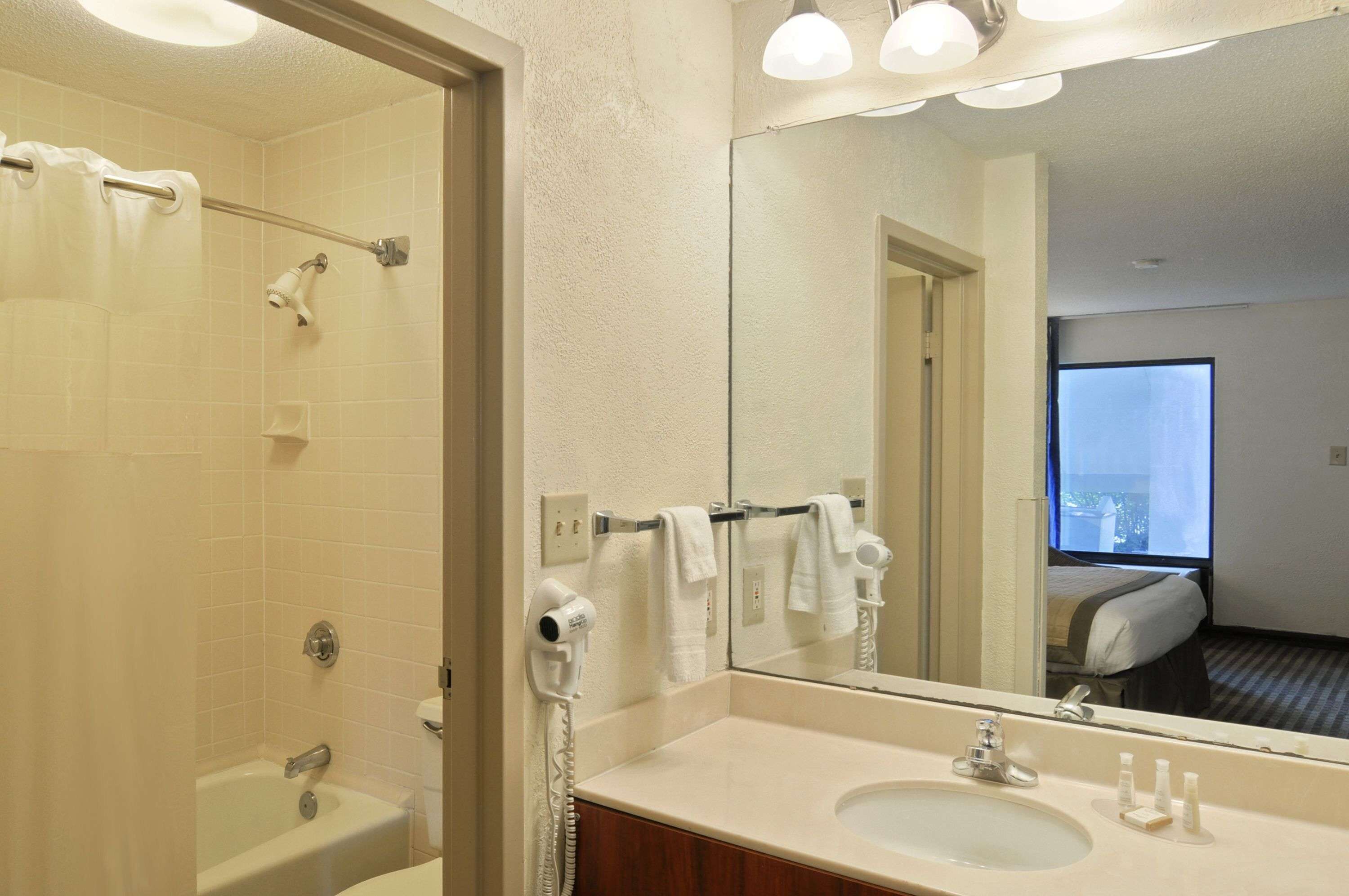 Une salle de bain d’hôtel équipée d’une baignoire, d’un lavabo, d’un miroir et d’un sèche-cheveux.