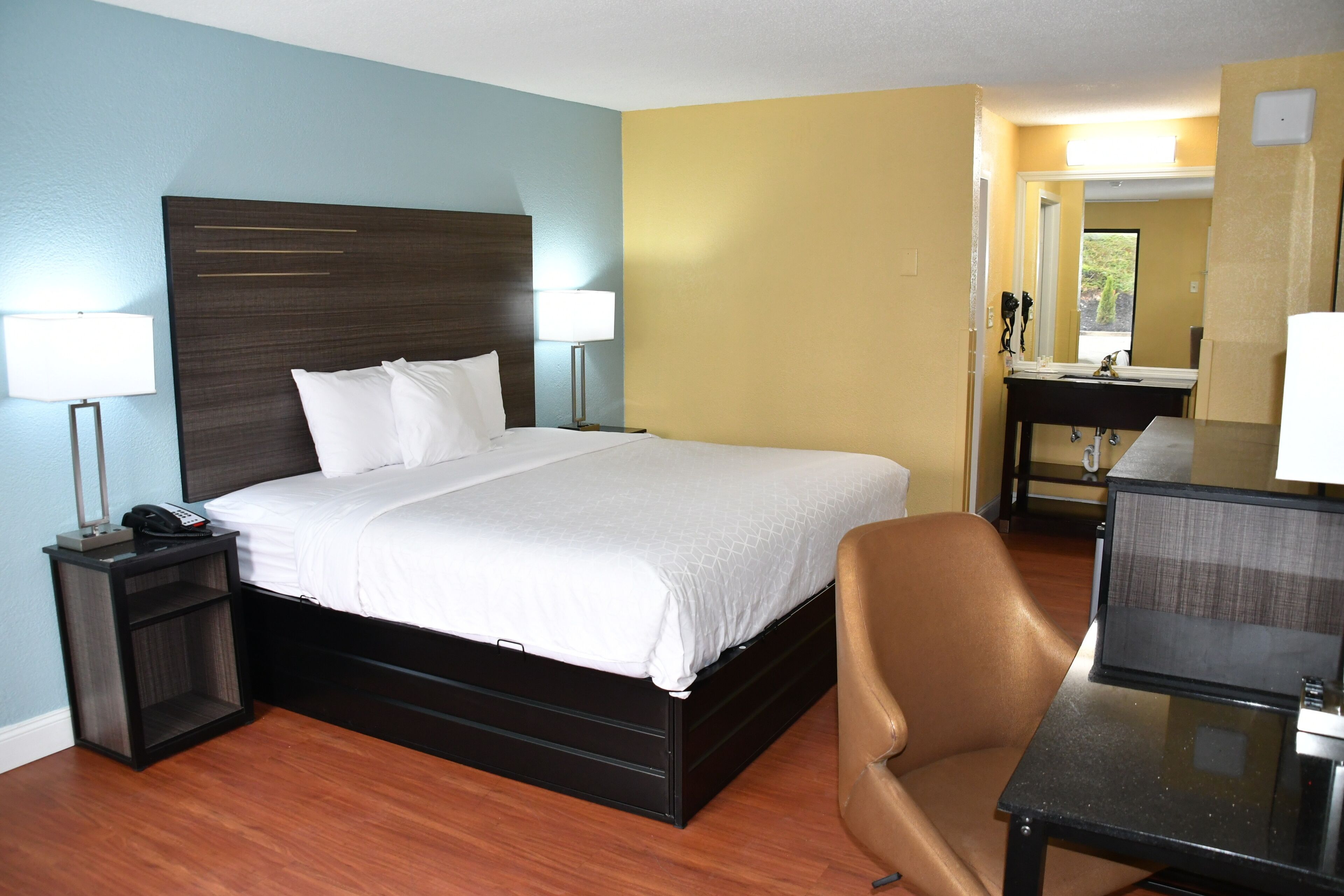 Quarto de hotel com cama, luminárias de cabeceira, escrivaninha e uma cadeira.