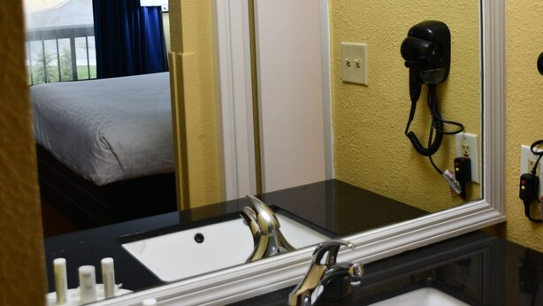A hotel bathroom with a large mirror, two sinks, and a hairdryer mounted on the wall.