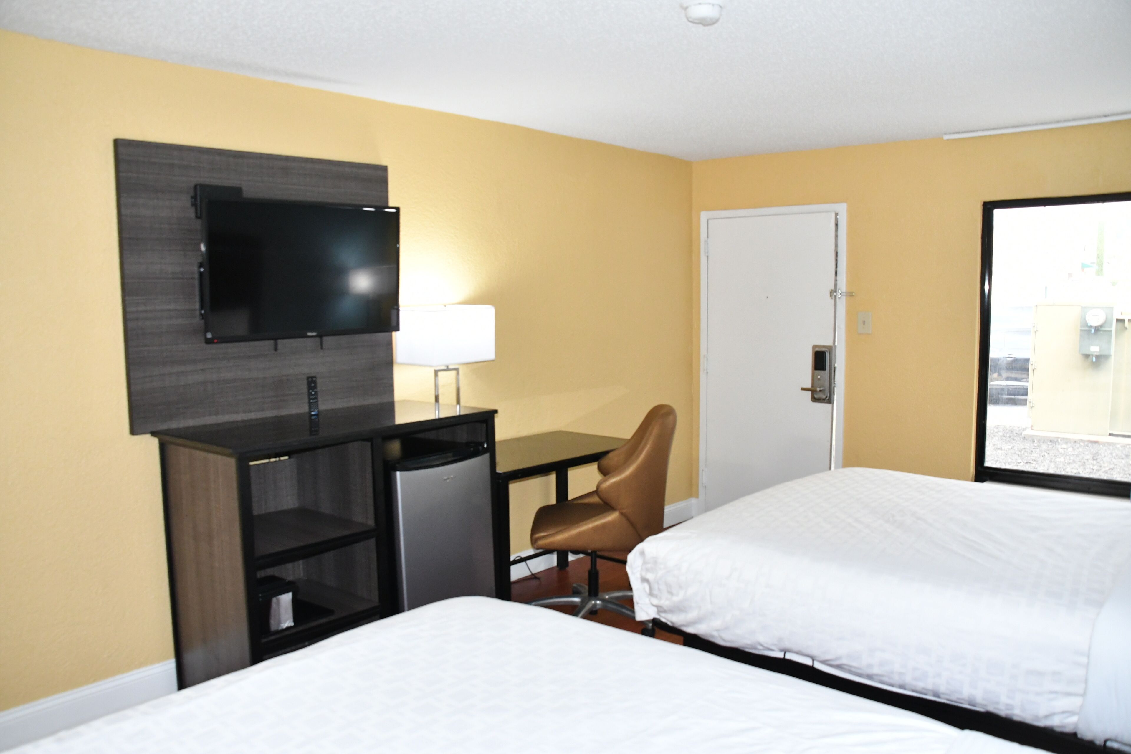 A hotel room with two beds, a desk with a chair, a television mounted on the wall, and a door leading to the outside.