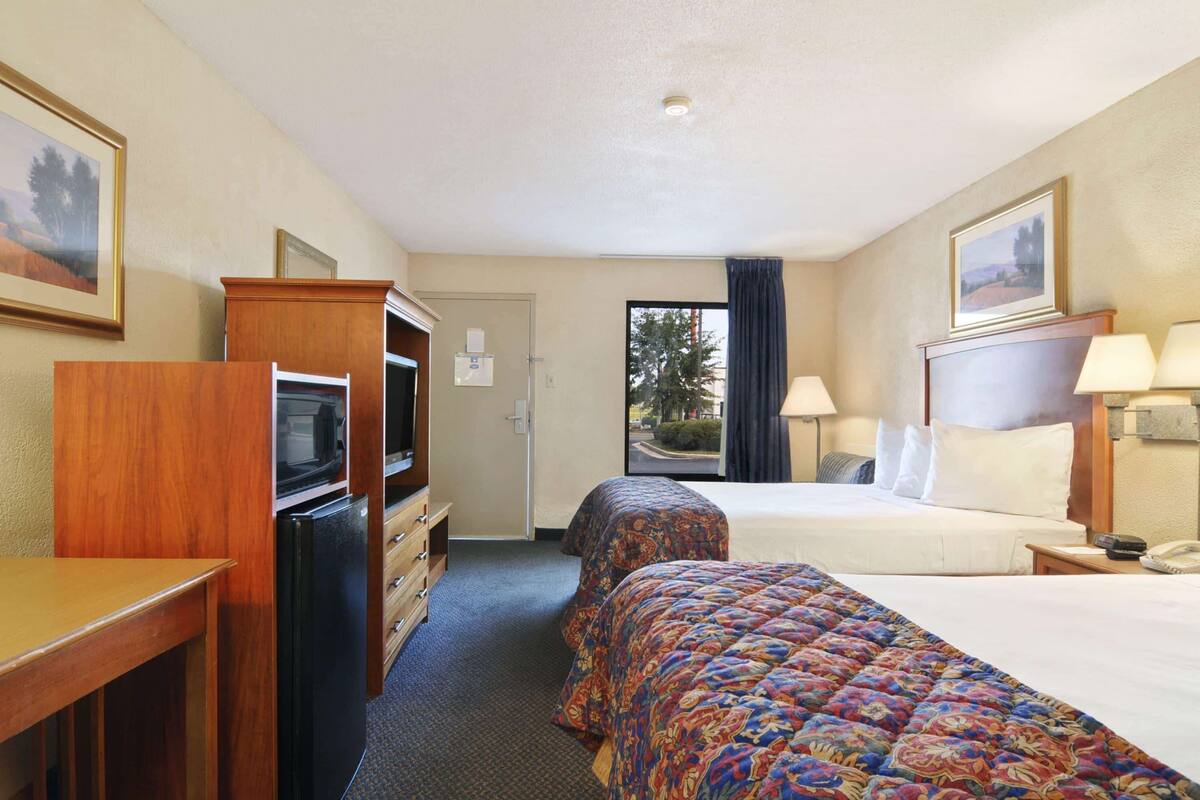 A hotel room with a bed, a desk, a TV, and a refrigerator.