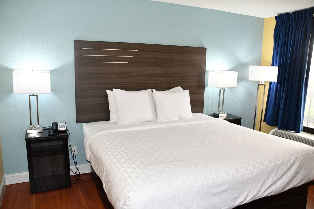 A hotel room with a large bed, two bedside tables, a desk, and a lamp.