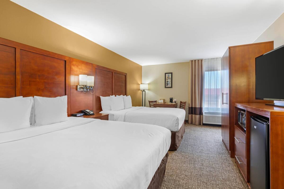 A hotel room with two beds, a desk, a television, and a minibar.