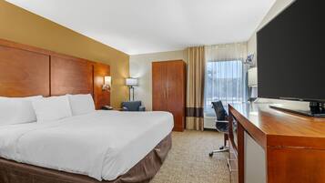 A hotel room with a large bed, a desk with a television, a wardrobe, and a window with curtains.