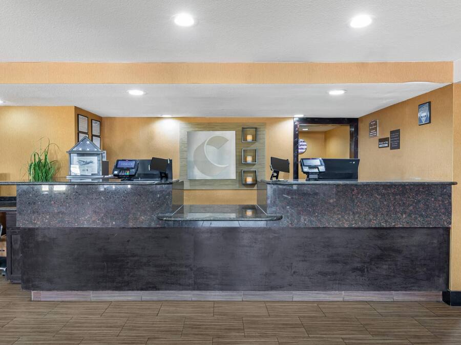A reception area with a marble counter, two computer stations, a plant, and framed certificates on the wall.