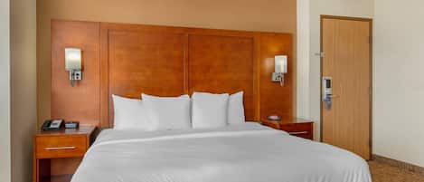 Une chambre d’hôtel avec un grand lit, une tête de lit en bois, des lampes de chevet, une table de chevet et une porte.