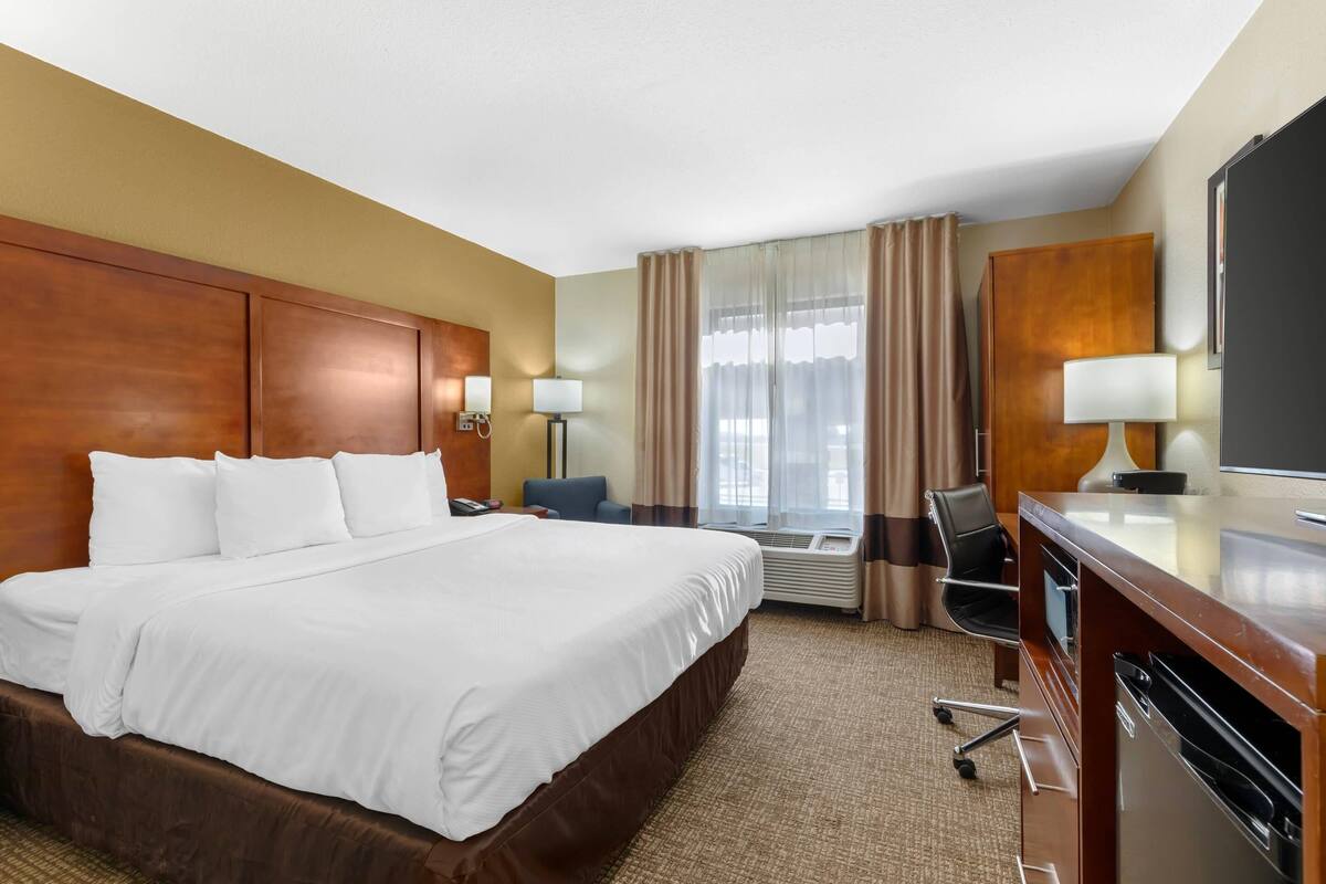 A hotel room with a large bed, a desk with a computer, a chair, and a TV.